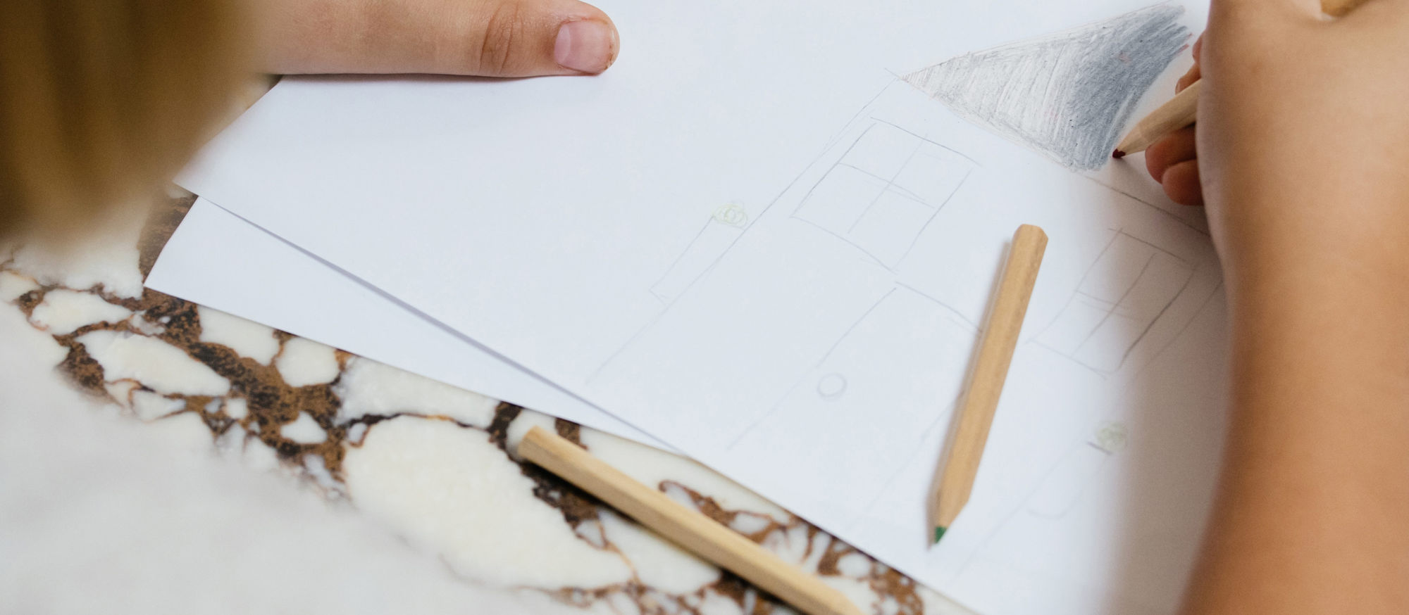 Hands sketching a plan on paper at a marble desk
